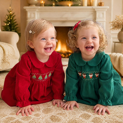 Two toddler girls wearing red and green Christmas Corduroy Dresses by a cozy holiday fireplace