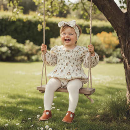 Baby wearing a Cream bloom floral romper set and matching headband on a swing outdoors.