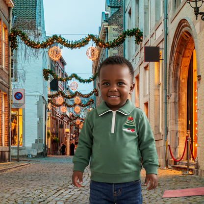 Toddler boy wearing the Little Evergreen Christmas Tree Quarter-Zip Pullover in green on a festive cobblestone street decorated with warm Christmas lights