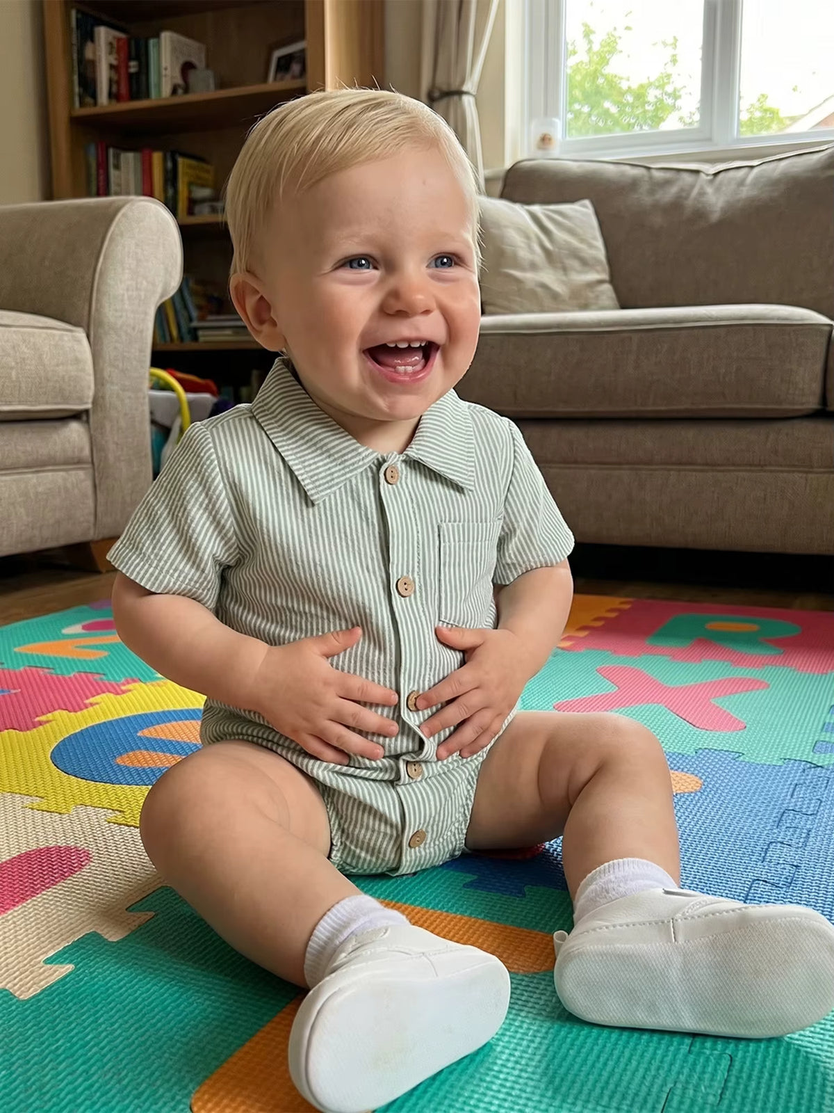Baby wearing a sage green striped cotton romper sitting on a colorful play mat.