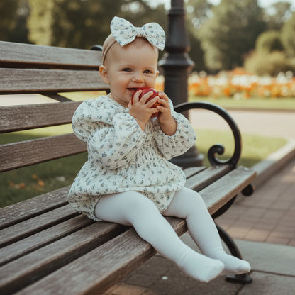 Baby wearing a sage bloom floral romper set with matching headband, sitting on a park bench.