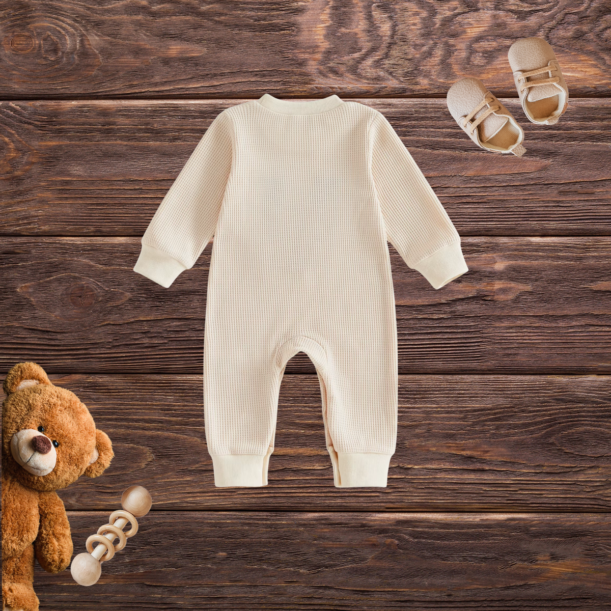Back view of cream waffle-textured baby reindeer romper showing long sleeves, round neckline and full-length legs on a rustic wooden background