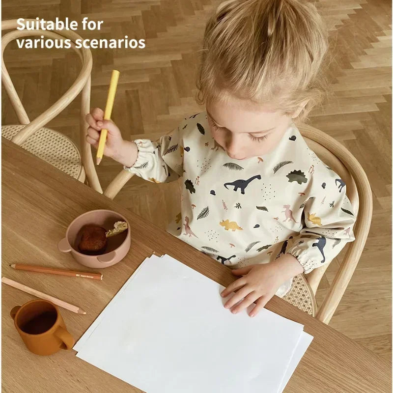 Child wearing Dinosaur waterproof long sleeve bib while drawing at a table