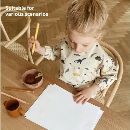 Child wearing Dinosaur waterproof long sleeve bib while drawing at a table