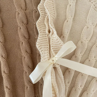 Close-up of cream and light brown cable-knit vests with side ribbon tie