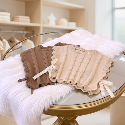 Cream and light brown girls’ cable-knit vests displayed on a gold table