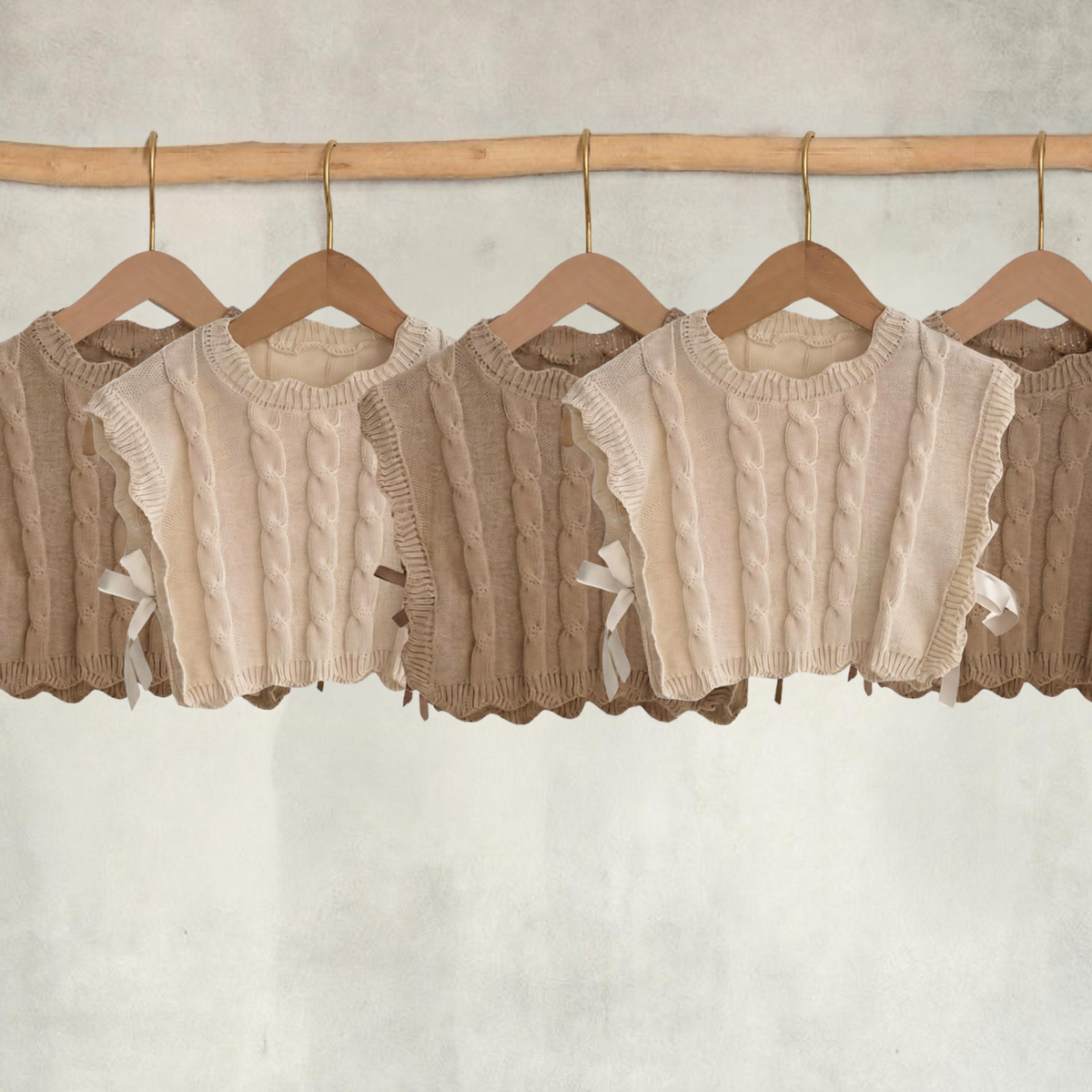 Cream and light brown girls’ cable-knit vests hanging on wooden hangers