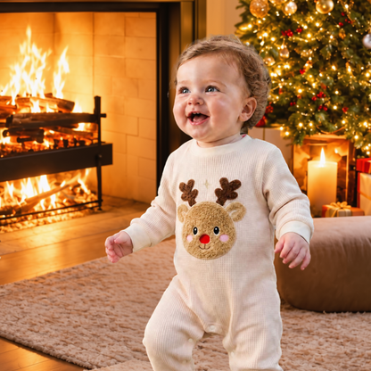 Happy baby standing beside a Christmas tree and glowing fireplace wearing a cream long-sleeve reindeer romper with a textured Rudolph appliqué