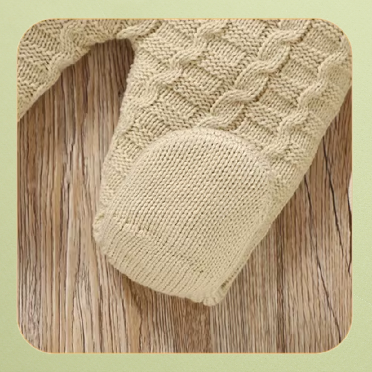 Close-up of footed cream knit baby overalls with cable knit pattern