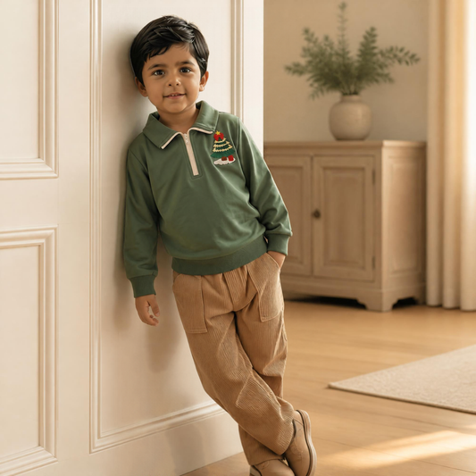 Toddler boy wearing the Little Evergreen Christmas Tree Quarter-Zip Pullover in green, leaning against an ivory paneled wall in a cozy neutral room