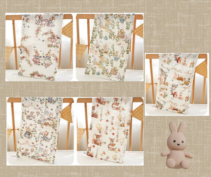 “Assorted luxury muslin baby burp cloths in woodland animal and floral prints, displayed hanging on a crib with soft toy bunny – breathable 6-layer cotton gauze perfect for newborn care.”