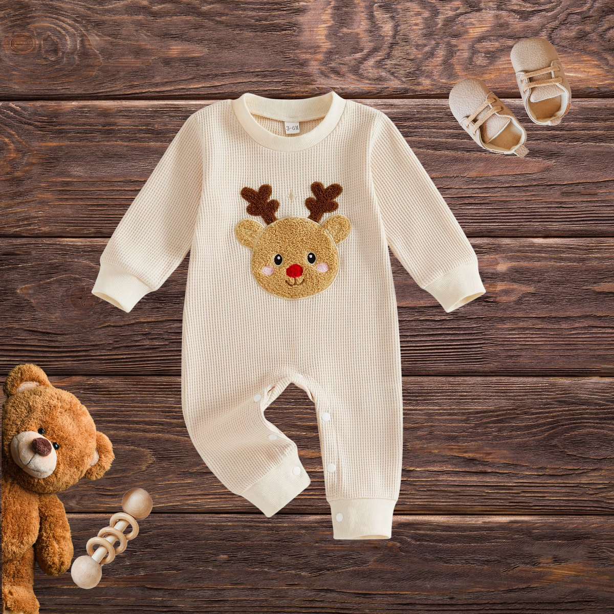 Front view of cream long-sleeve waffle-textured baby romper with raised Rudolph reindeer appliqué and snap closures, styled on a wooden background