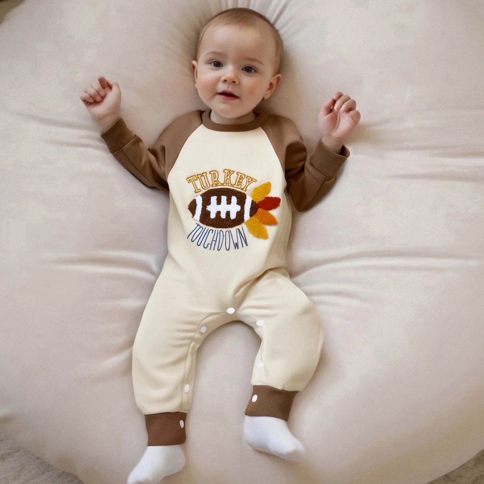 "Smiling baby wearing brown and cream romper with turkey and football design, holiday outfit"