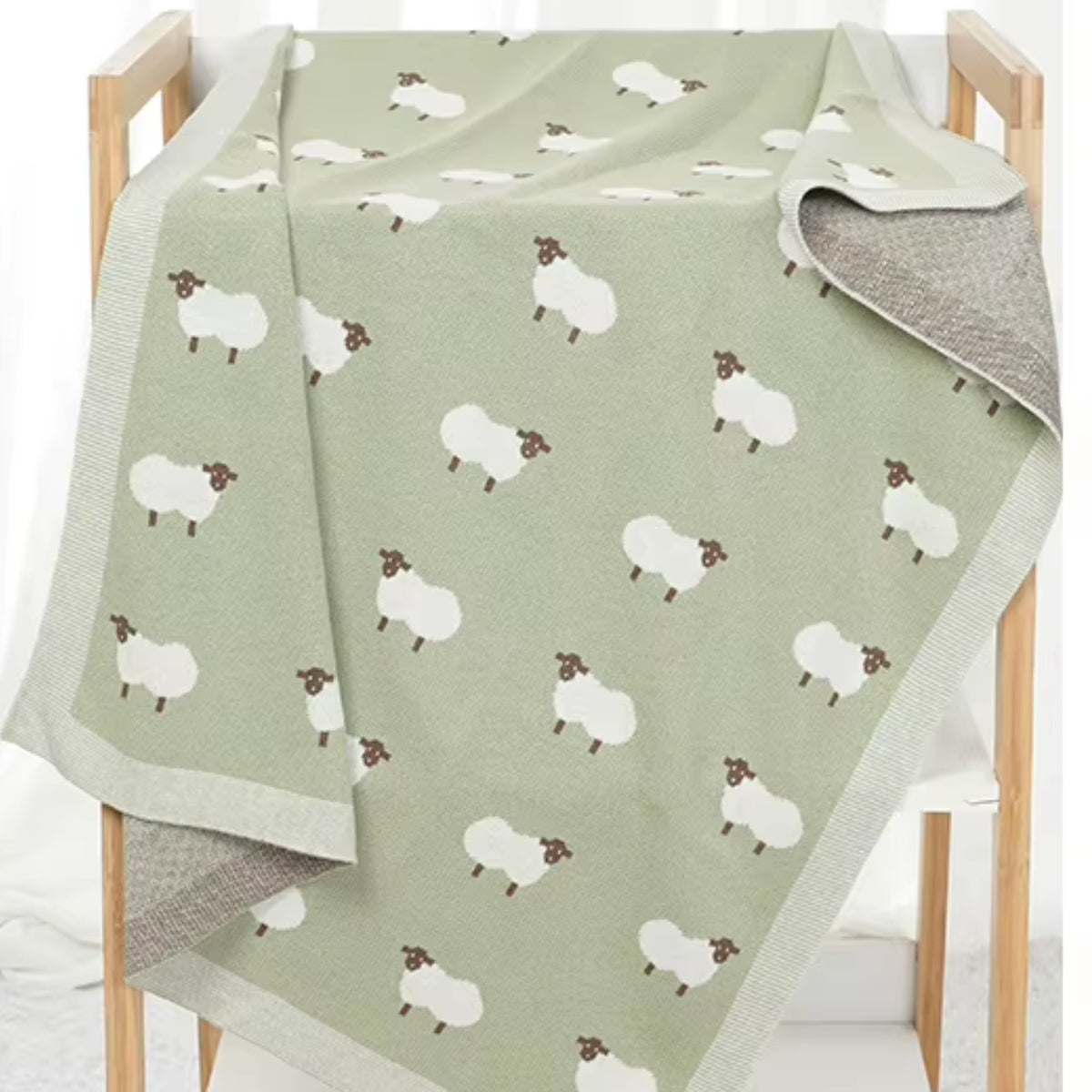 Sage green sheep baby blanket draped over wooden display rack