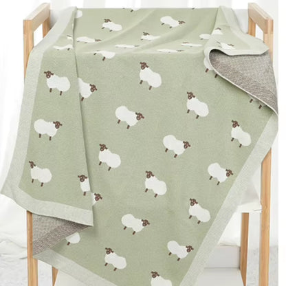 Sage green sheep baby blanket draped over wooden display rack