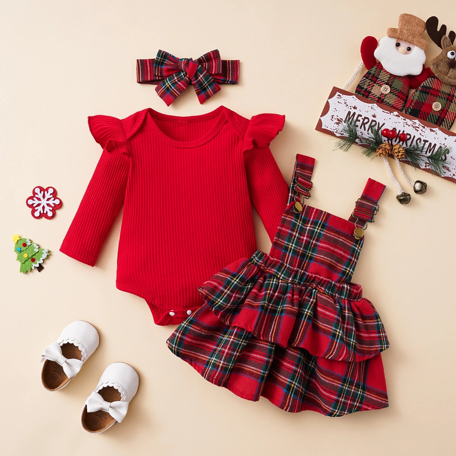 1. Flat lay of red ruffle baby romper and plaid suspender dress set with bow headband, Christmas outfit for girls.

2. Plaid Christmas baby outfit set – romper, plaid suspender skirt, and bow headband arranged on beige background.