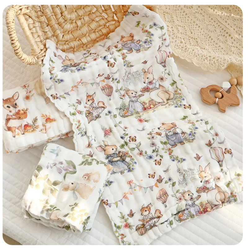 “Luxury muslin baby burp cloths with whimsical woodland animal prints, styled flat with natural wicker basket, knit blanket, and wooden teether – ultra-soft 6-layer cotton gauze perfect for newborn essentials.”