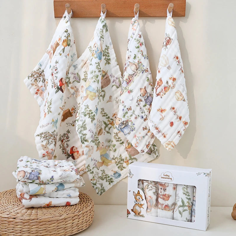 “Set of luxury muslin baby burp cloths in whimsical woodland animal prints, displayed hanging on wooden hooks with gift box and folded cloths – soft, breathable cotton gauze for newborn care and gifting.”
