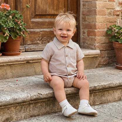 Smiling baby wearing a beige striped cotton romper sitting on stone steps.