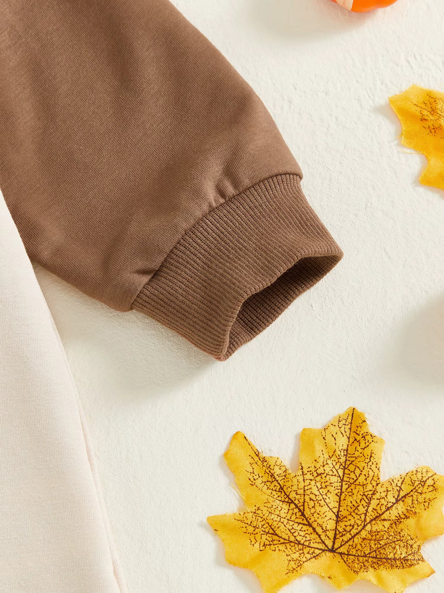 "Close-up of cotton fabric sleeve in brown with fall leaves, detail of Thanksgiving romper"